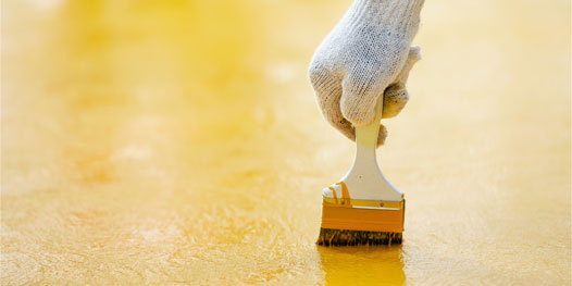 This image shows a man painting a floor using a paint brush.